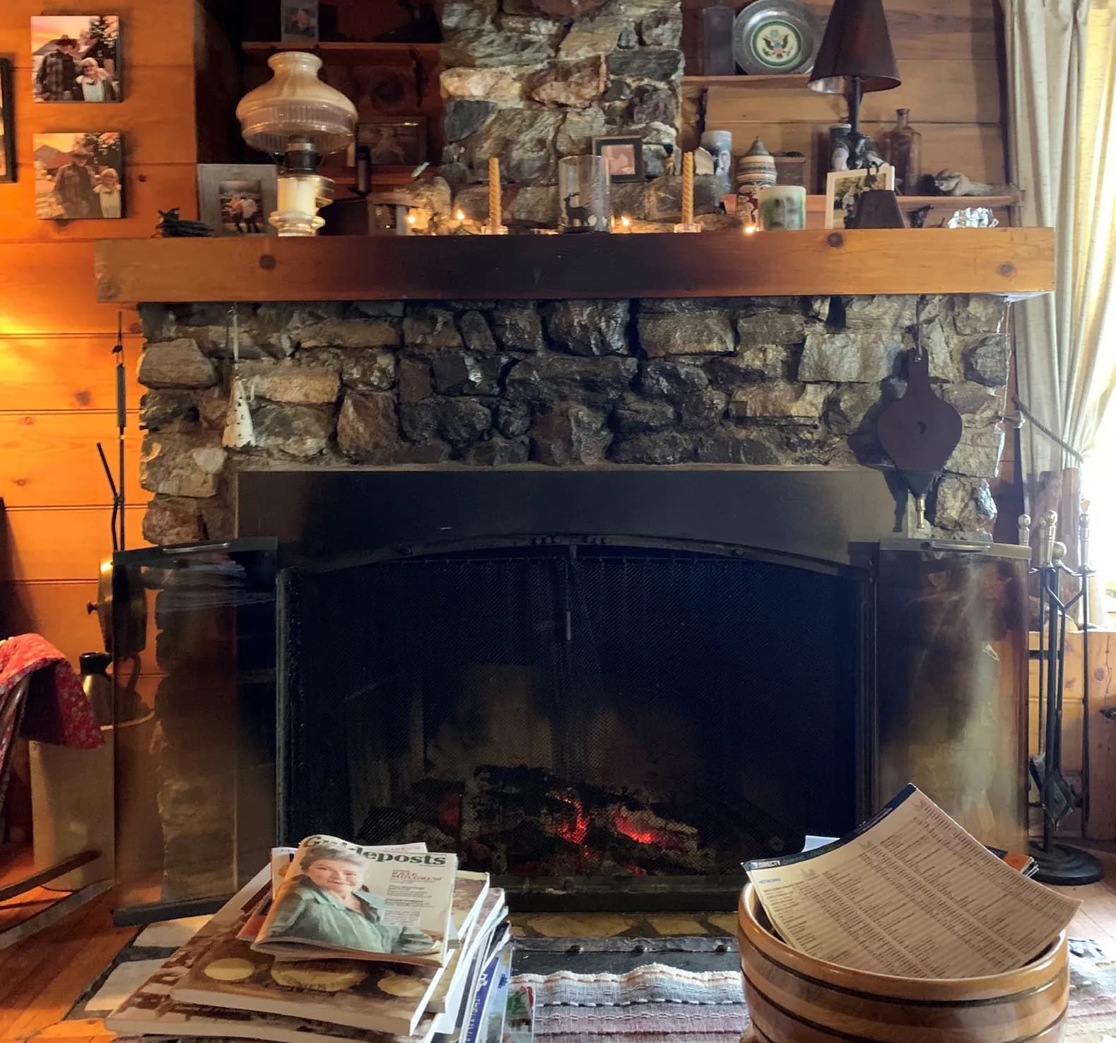 A stone fireplace with a low fire behind its screen, under a wooden mantel