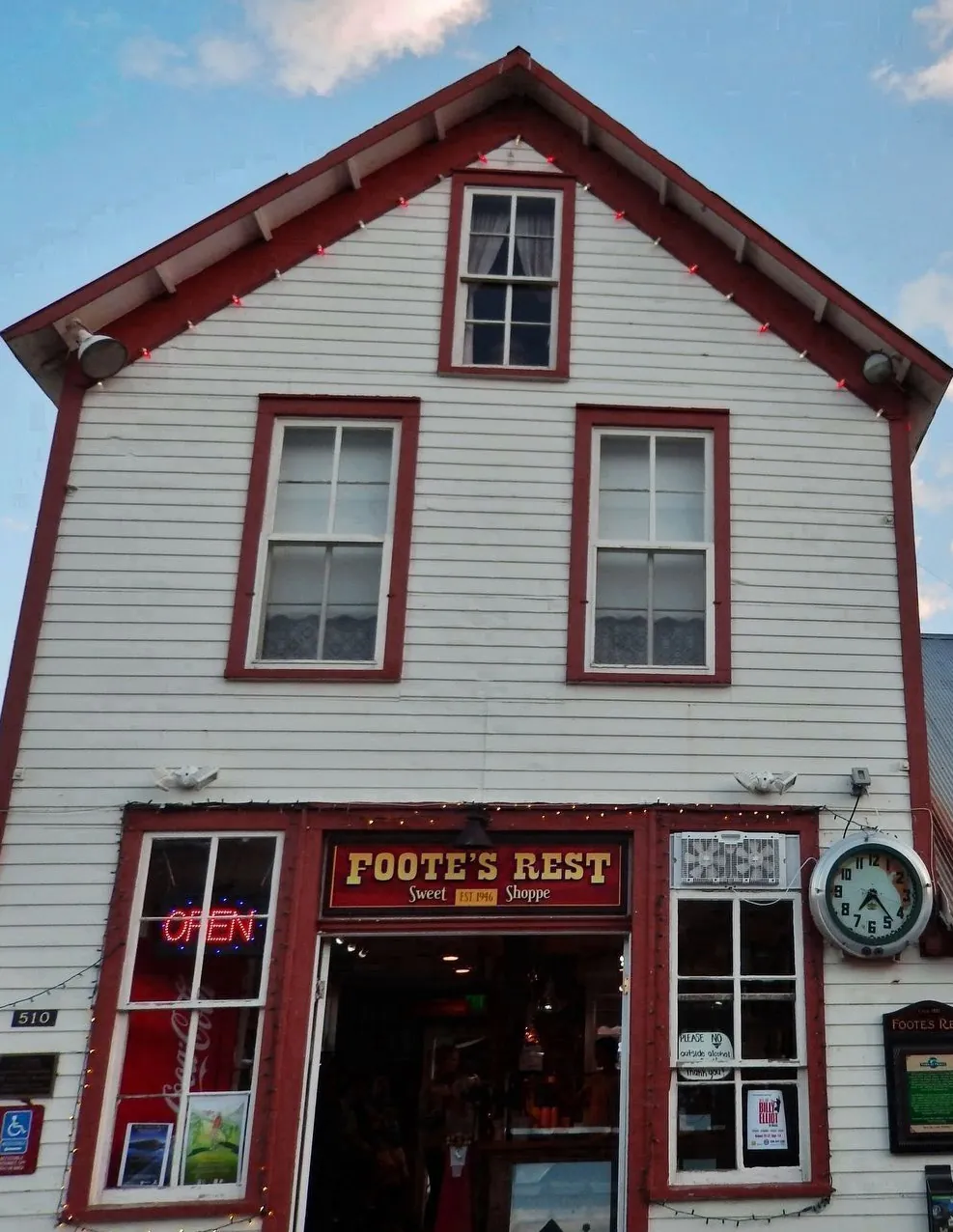 The front of the Foote's Rest Sweet Shoppe in Frisco, a white clapboard building with red trim, an open sign and a clock