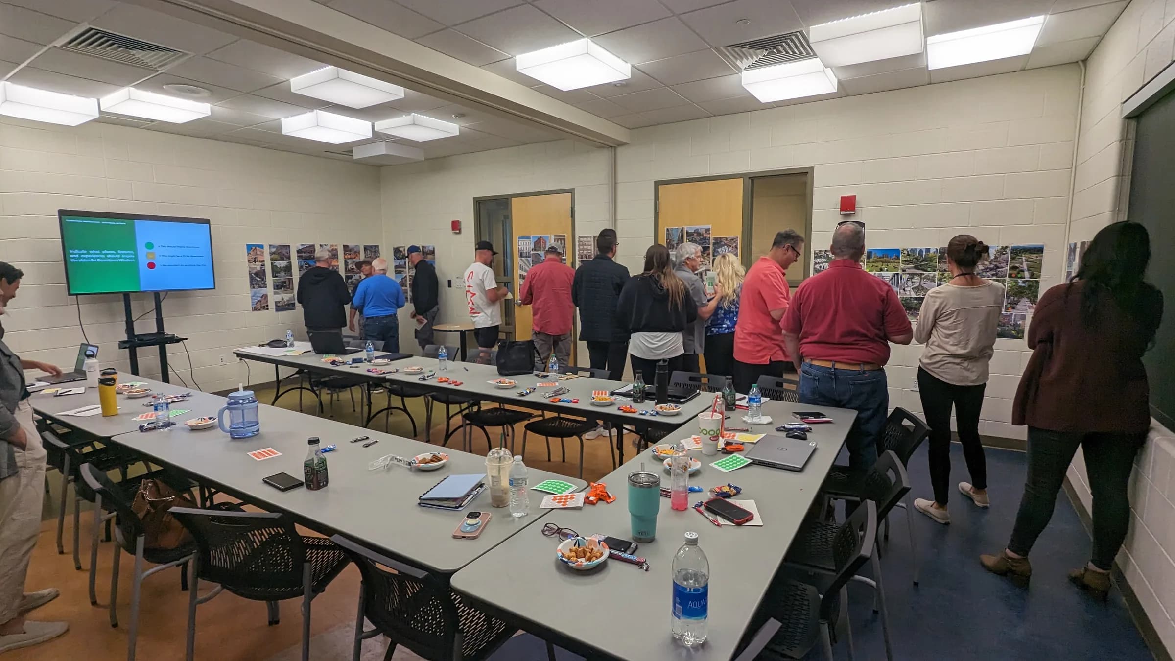 People walking a wall of photo boards during a planning session, with notes, markers and drinks left on the long tables