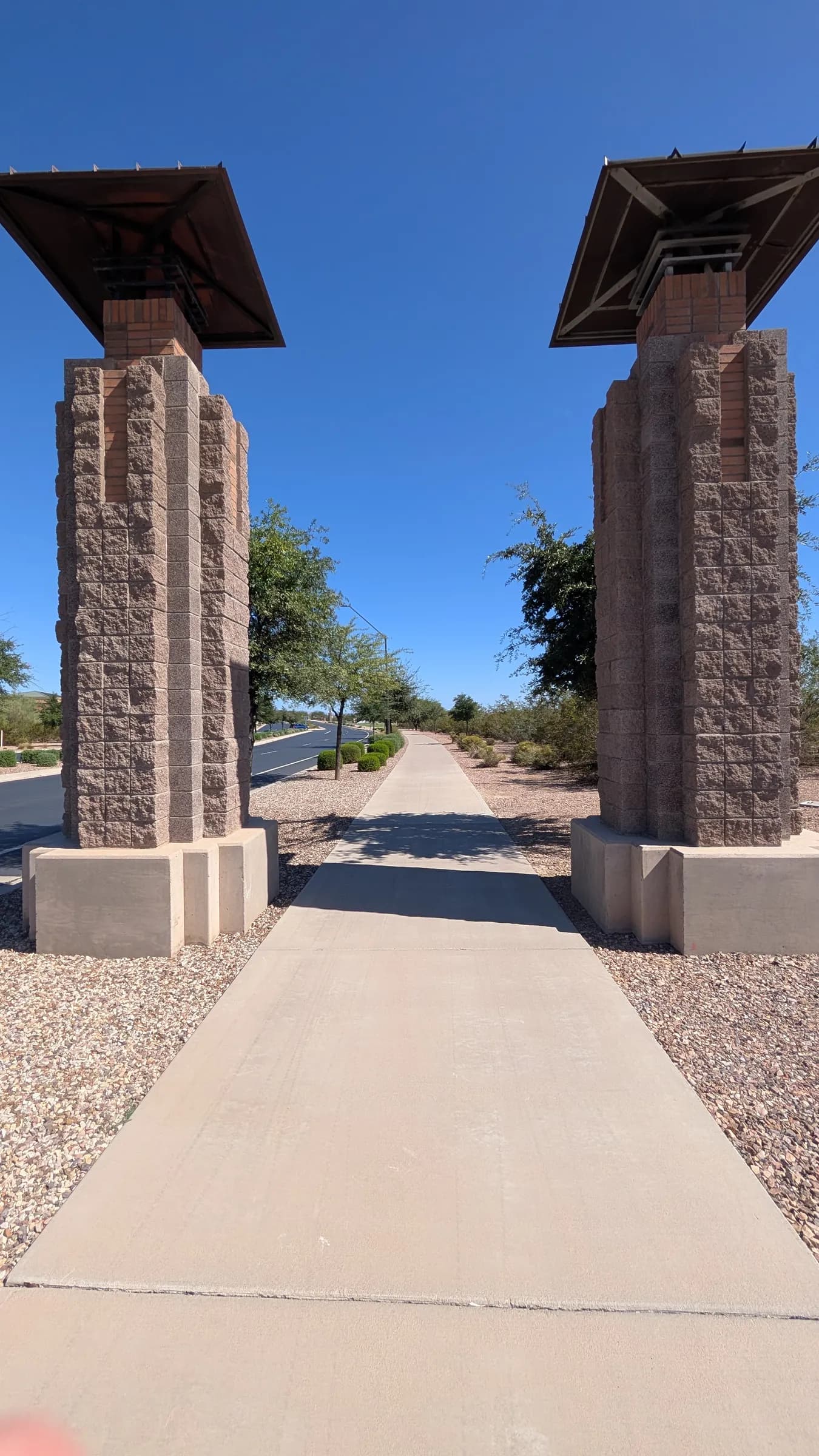 A concrete trail running between two tall masonry pillars at Anthem at Merrill Ranch, under a clear blue sky