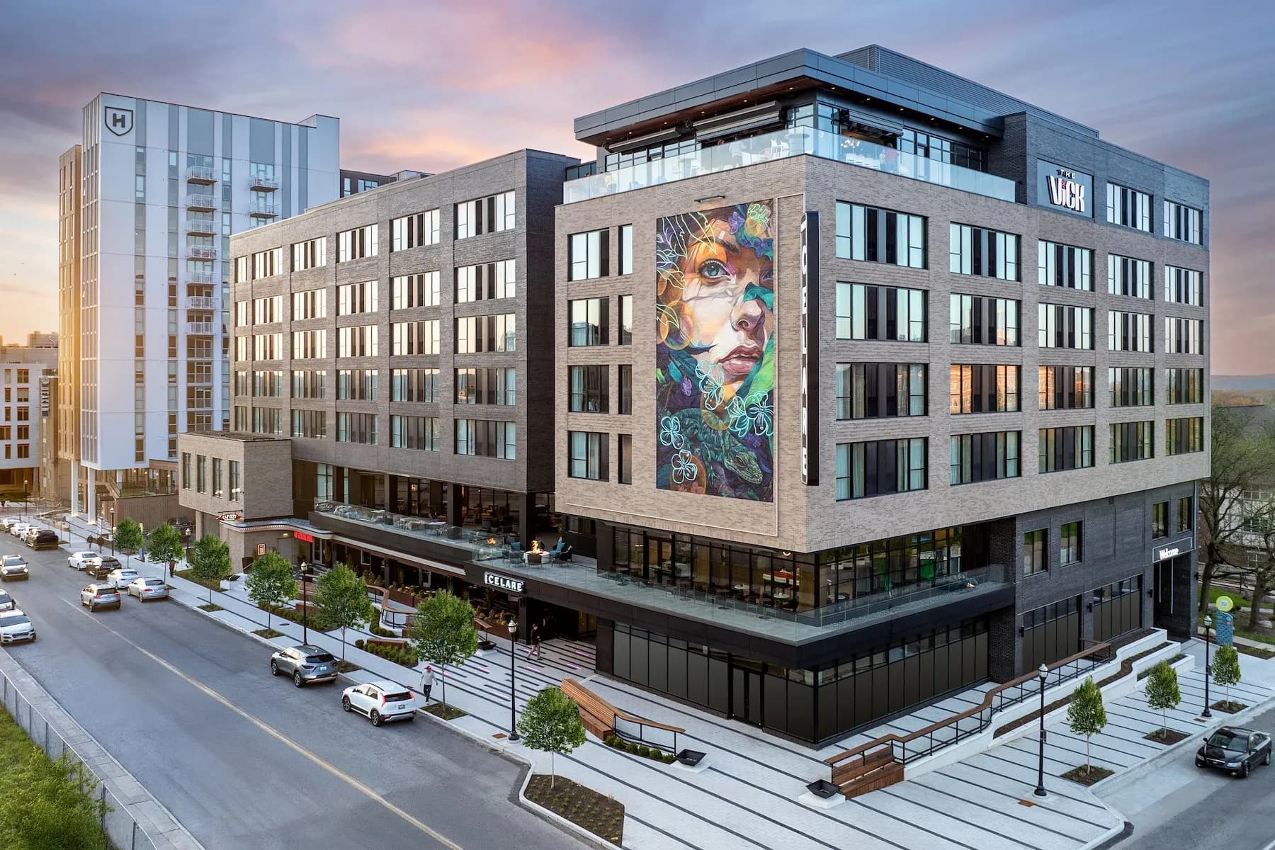 Hotel Celare at dusk, seen from above the street, with its name over the entrance and down the corner of the building and a mural on its side
