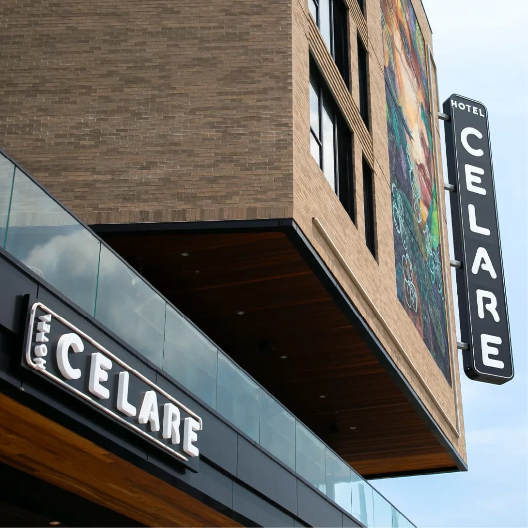 Looking up at Hotel Celare, with its name on a tall corner sign beside the edge of a painted mural, and again over the entrance