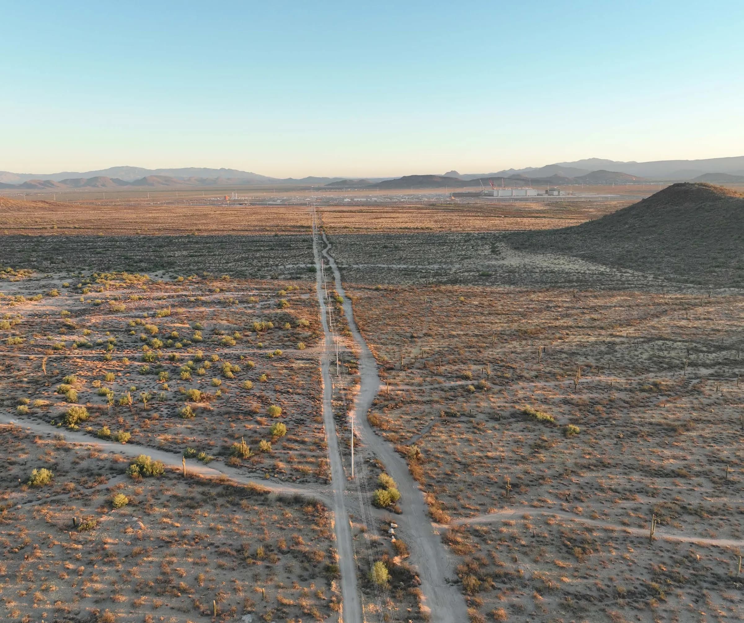 The North Phoenix desert from the air in low sun, with dirt tracks running toward the mountains